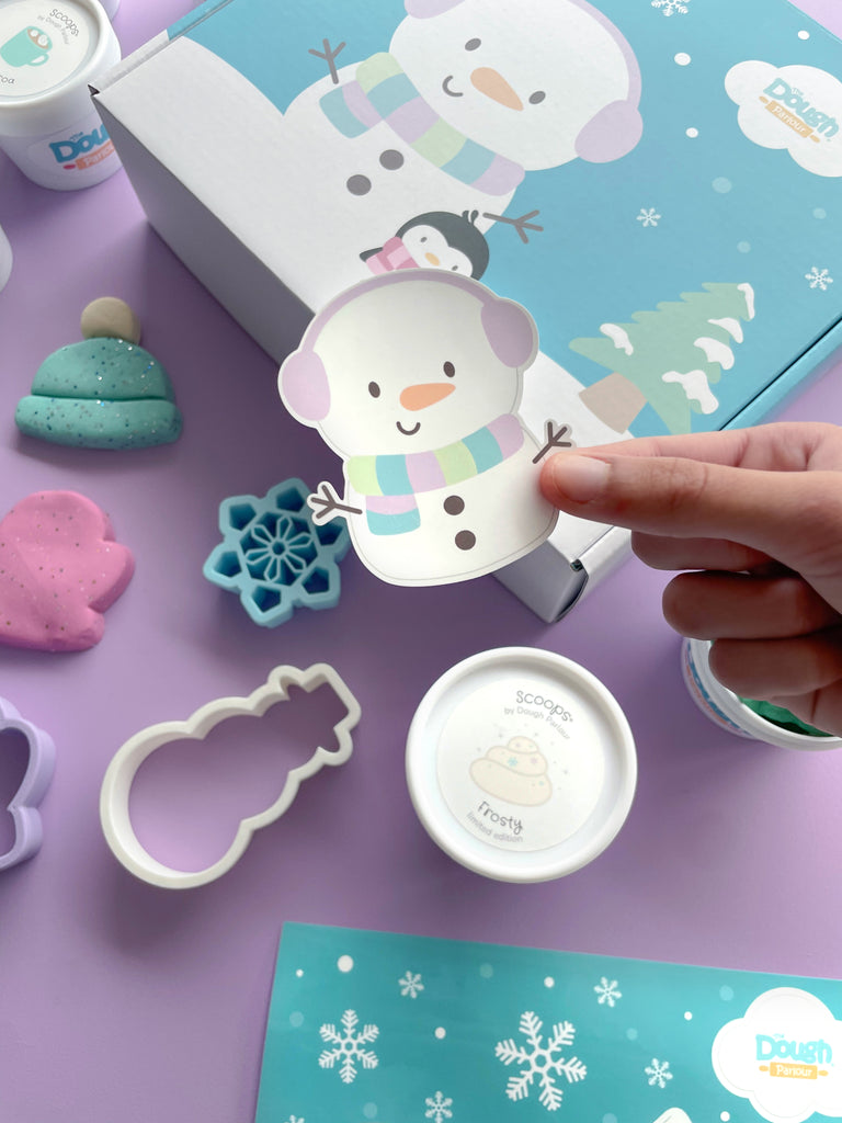 Frosty Playbox sticker with closed lid, dough, cutters in the background on a purple table