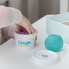 little hand digging into grape scented dough in tub beside ball of blue dough on white table