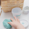 little hand playing with blue cotton candy scented dough beside empty tub and wicker basket on a white table