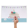 Birthday mat printing shows purple and green bunting and a cake on a cake plate sitting on a blue table. A child's hand has a modelling dough strawberry placed over the printed cake image