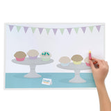 Birthday mat printing shows green and purple bunting with two cake plates holding three cupcakes on each, sitting on a blue table. A child's hand holds a modelling dough candle they placed over one cupcake