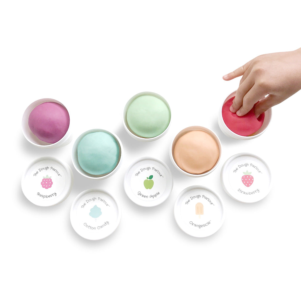 Five tubs of dough without lids showing the different colours and a child's hand squishing the dough in one tub