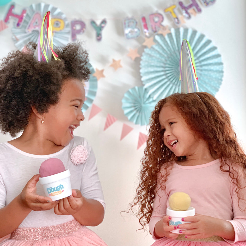 Two little girls at a birthday party holding tubs of dough