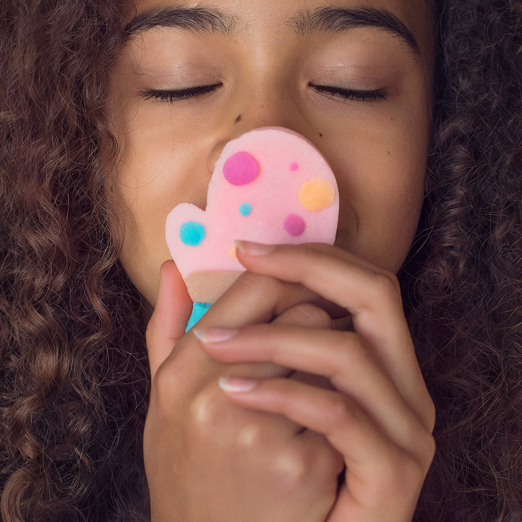 Child smelling pink mitten with dots sculpted out of dough